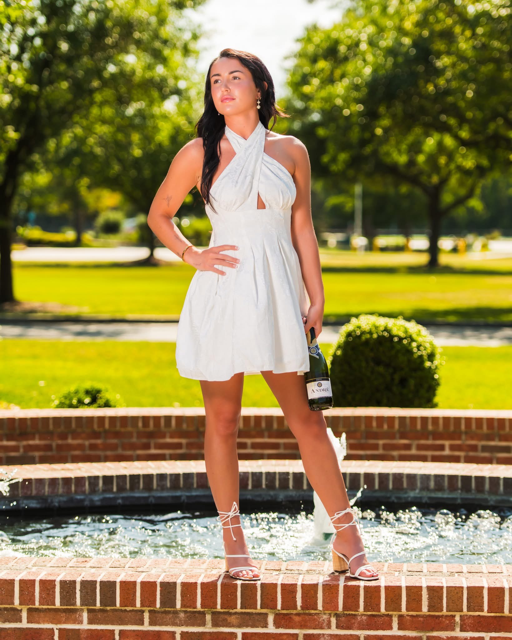 A woman in a white dress standing beside a fountain with one hand on her hip
