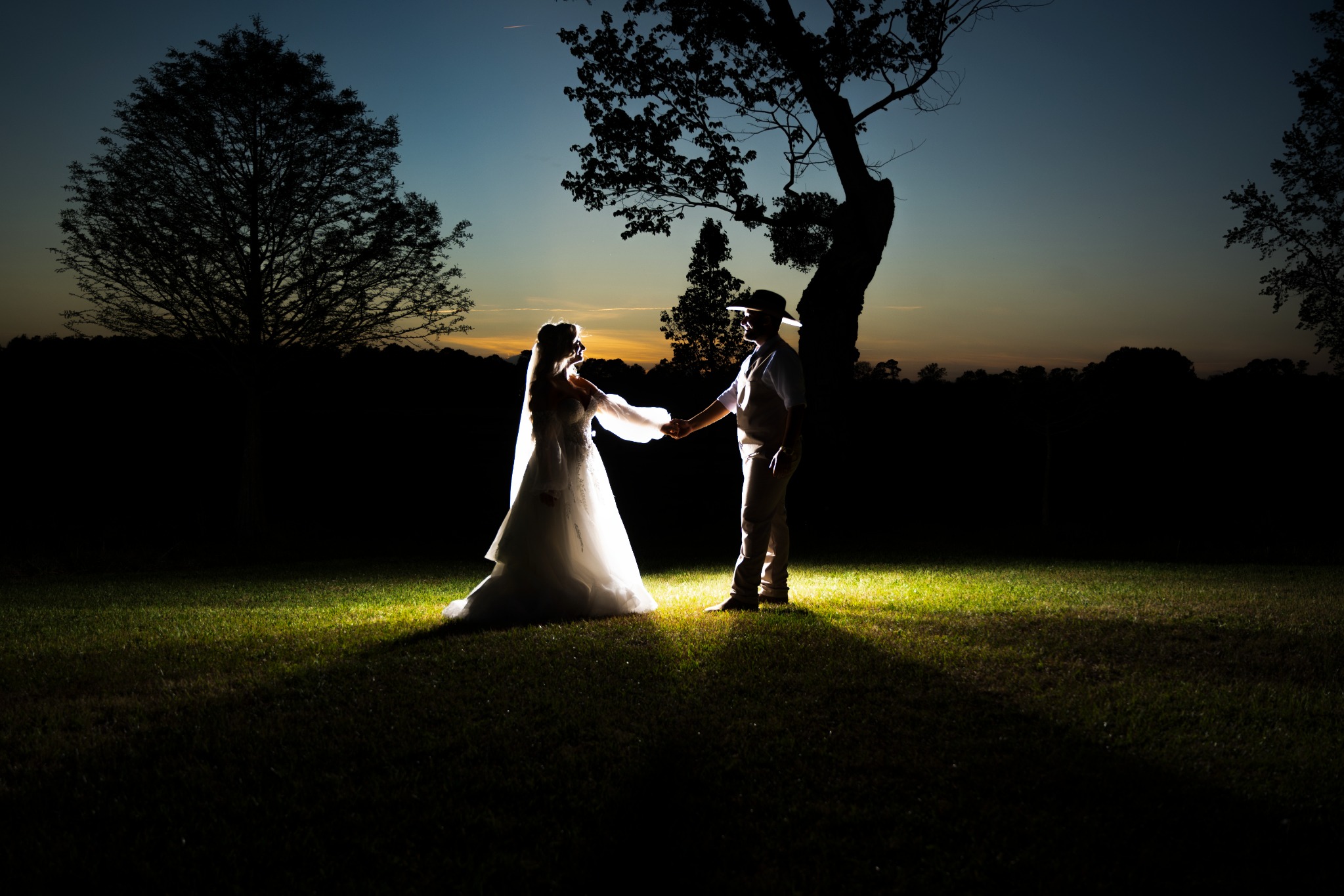 Newlyweds holding hands in a dramatic field portrait after sunset at Wildhorse at Parker Farms